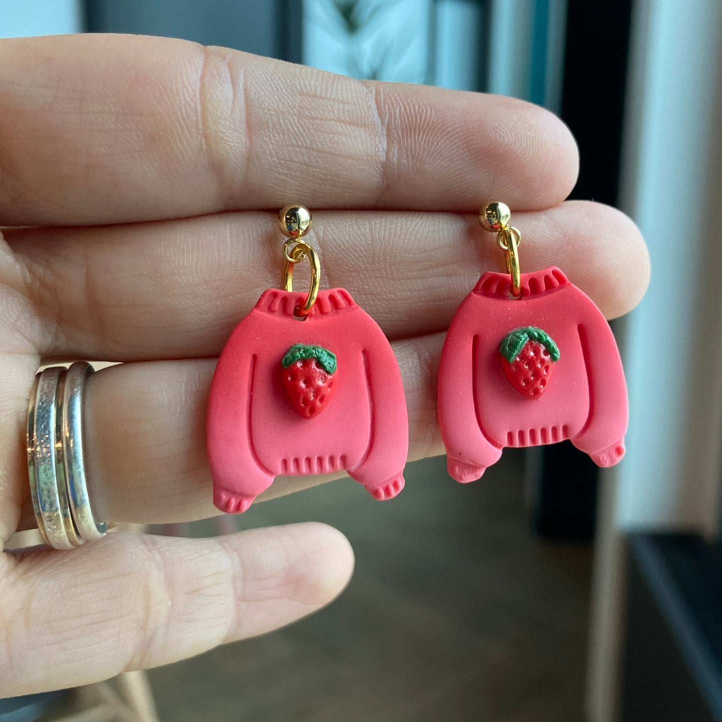 Boucles d'oreilles artisanales en argile polymÚre en forme de chandail rouge avec fraise sculptée, finition dorée hypoallergénique.