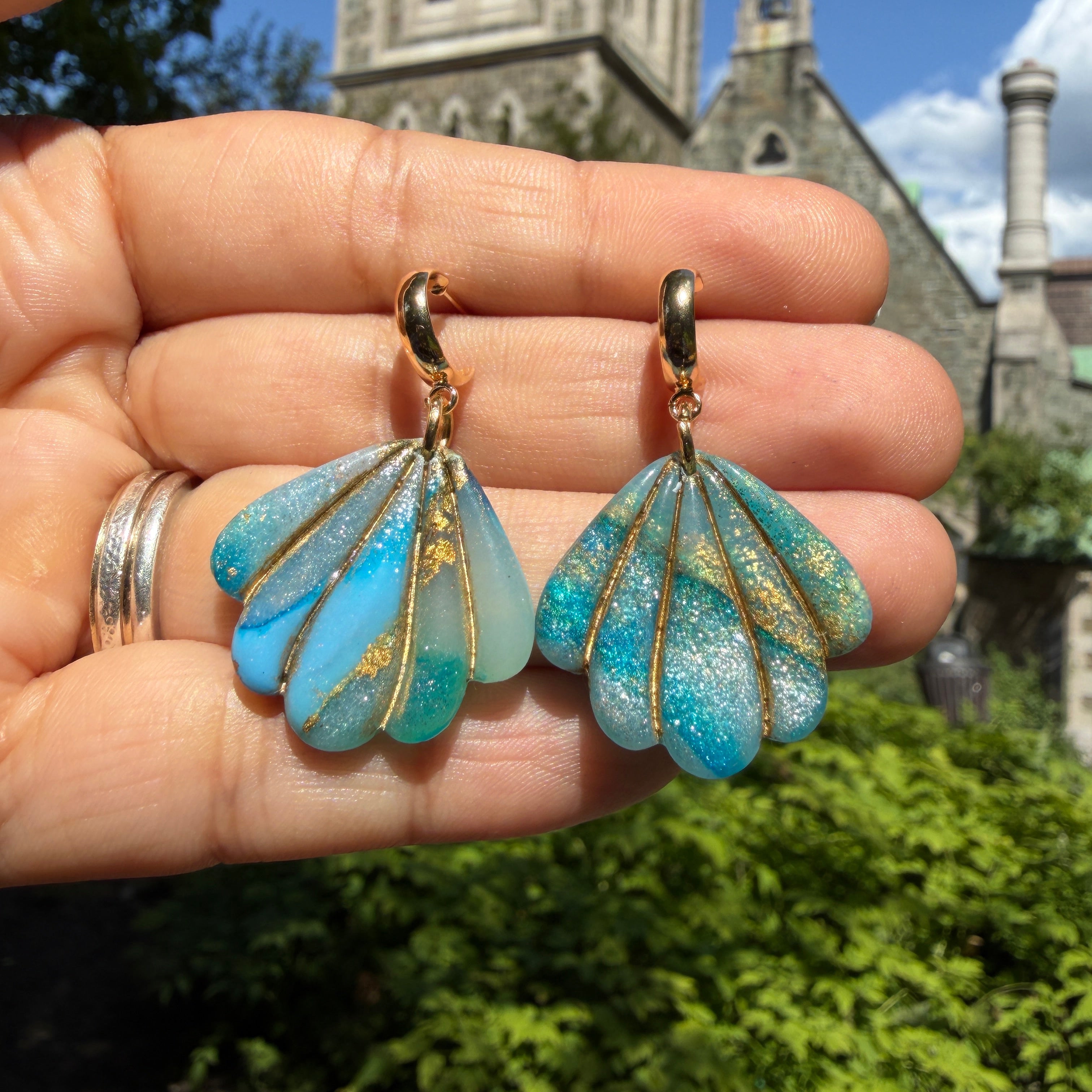 Boucles d’oreilles Laguna – Coquillage sculpté : coquillages turquoise et sable aux lignes dorées, tenus dans la main