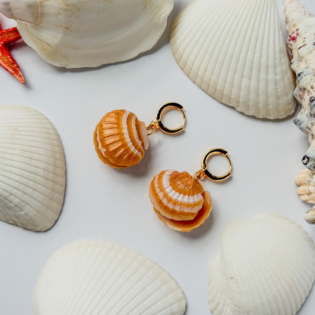 Boucles d’oreilles Perla del Mare – Coquillage à perle : coquillages orange ambré striés sur anneaux dorés, posés parmi des coquilles