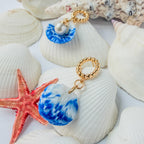 Boucles d’oreilles Galite – Perle d’écume : coquillages bleu et blanc avec perles, montrés de côté parmi des coquillages