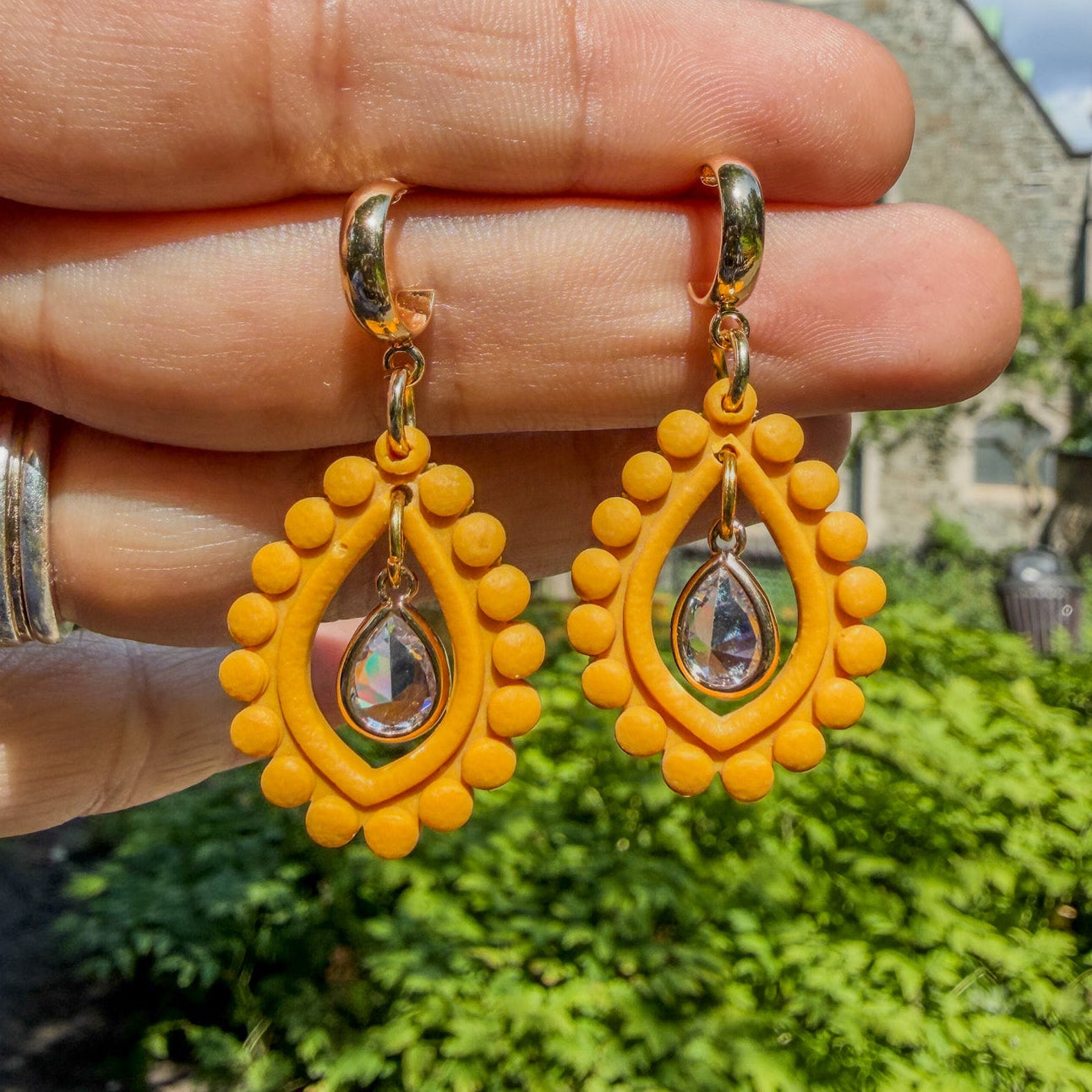 Boucles d’oreilles Qatra – Gouttes de lumière : pendentifs jaune safran bordés de perles d’argile et gouttes irisées, tenus dans la main