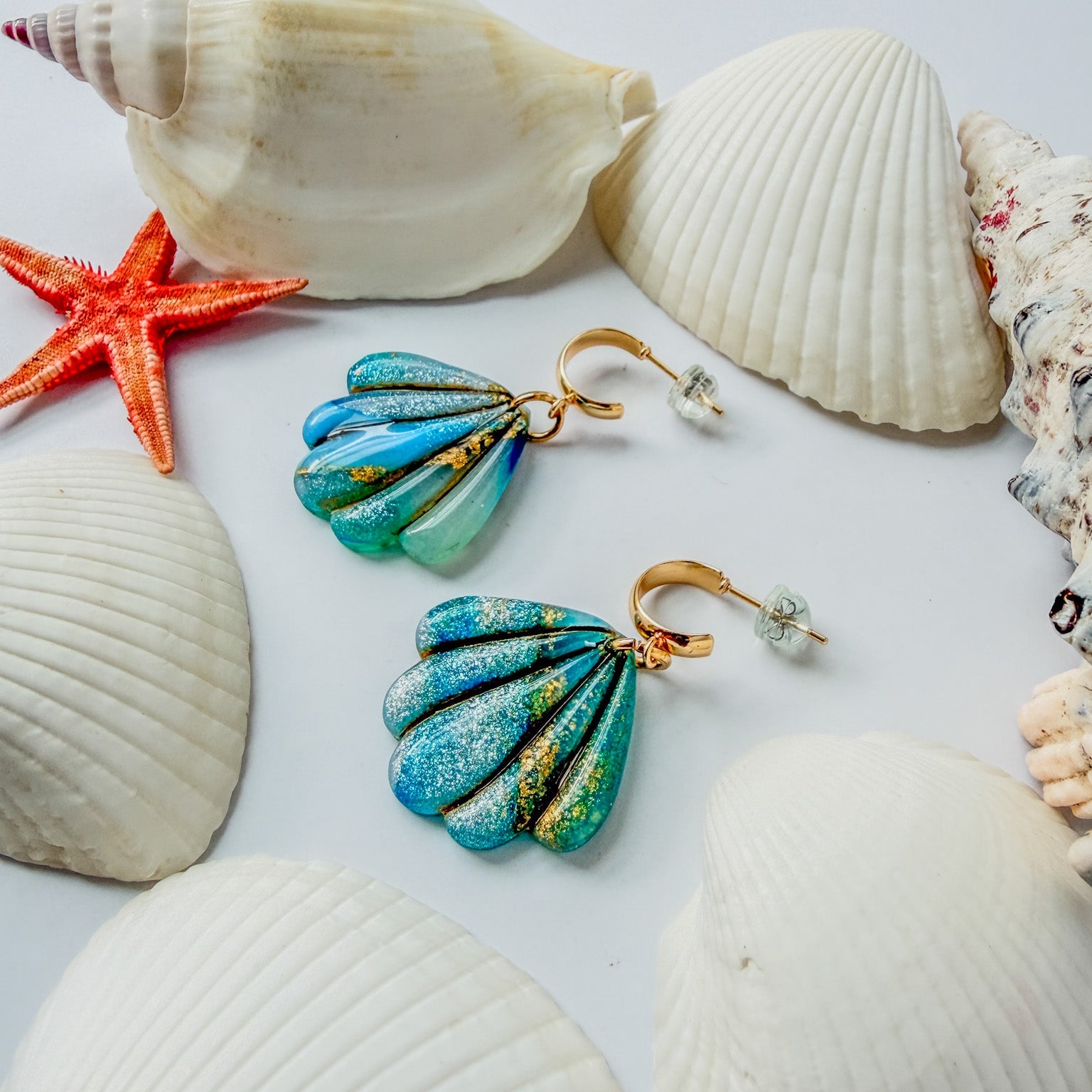 Boucles d’oreilles Laguna – Coquillage sculpté : coquillages bleu lagon marbrés d’or, posés parmi des coquillages