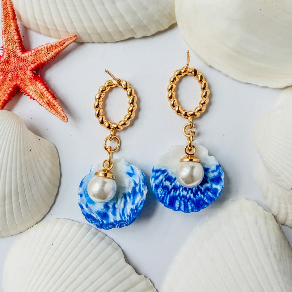 Boucles d’oreilles Galite – Perle d’écume : coquillages bleu et blanc avec perles nacrées et anneaux dorés, parmi des coquillages