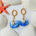 Boucles d’oreilles Galite – Perle d’écume : coquillages bleu et blanc avec perles nacrées et anneaux dorés, parmi des coquillages