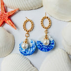 Boucles d’oreilles Galite – Perle d’écume : coquillages bleu et blanc avec perles nacrées et anneaux dorés, parmi des coquillages