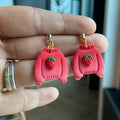 Boucles d'oreilles artisanales en argile polymère en forme de chandail rouge avec fraise sculptée, finition dorée hypoallergénique.