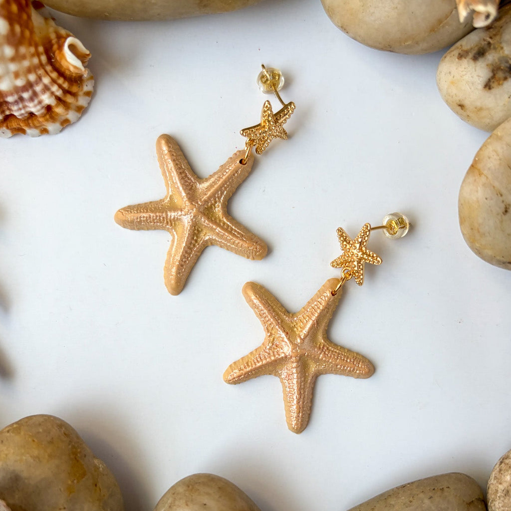 Boucles d’oreilles Étoiles de mer sculptées : étoiles de mer beige nacré avec attaches dorées, parmi coquillages et galets