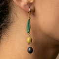Une boucle d’oreille portée, avec une feuille verte et deux olives, l’une verte et l’autre noire, suspendues à des chaînes dorées.