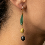 Une boucle d’oreille portée, avec une feuille verte et deux olives, l’une verte et l’autre noire, suspendues à des chaînes dorées.