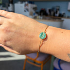 Bracelet Olea porté au poignet : médaillon rond vert orné d’un rameau d’olivier doré et fine chaîne de couleur dorée.