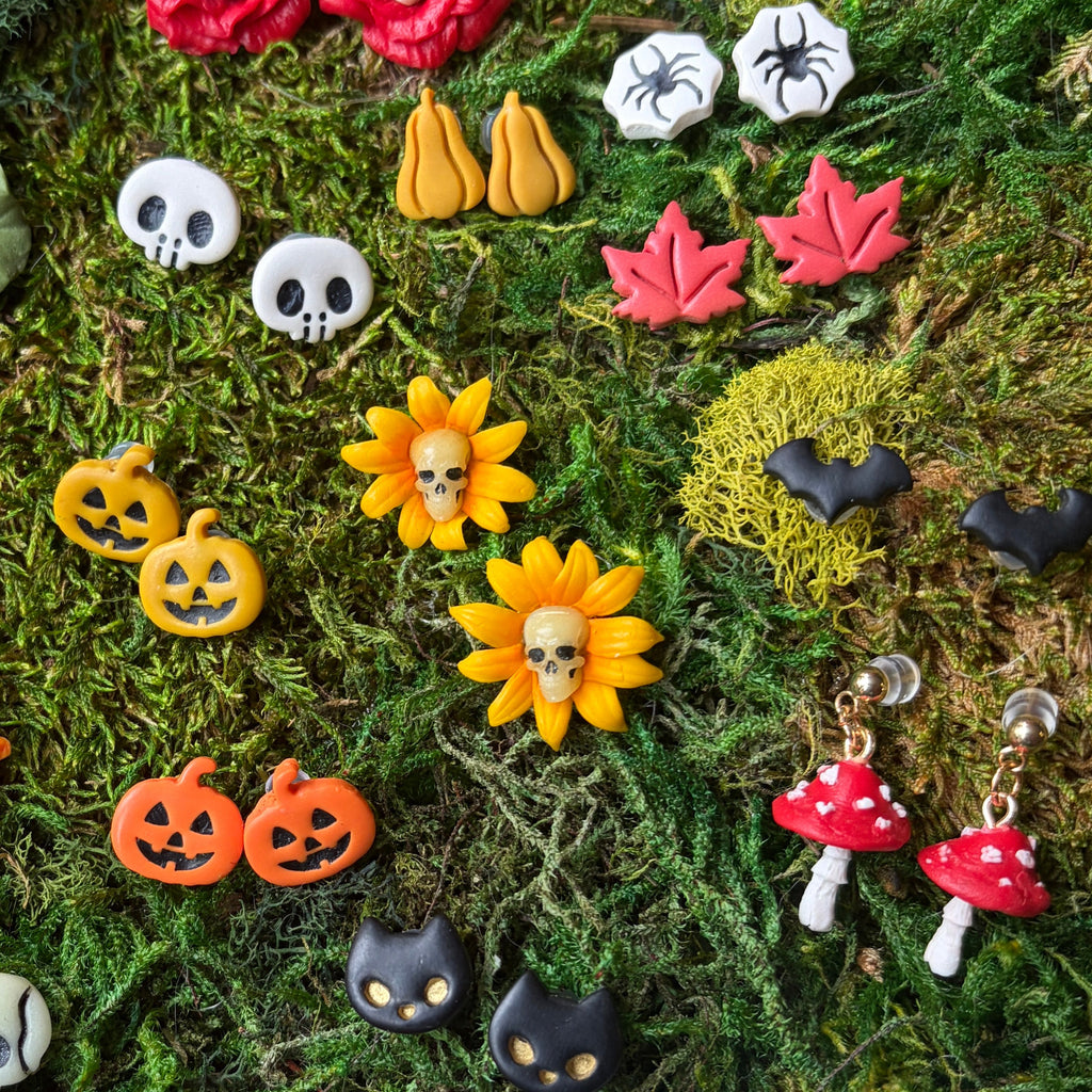 Sélection de bijoux d’Halloween sur la mousse, dont des tournesols jaunes à cœur de crâne.