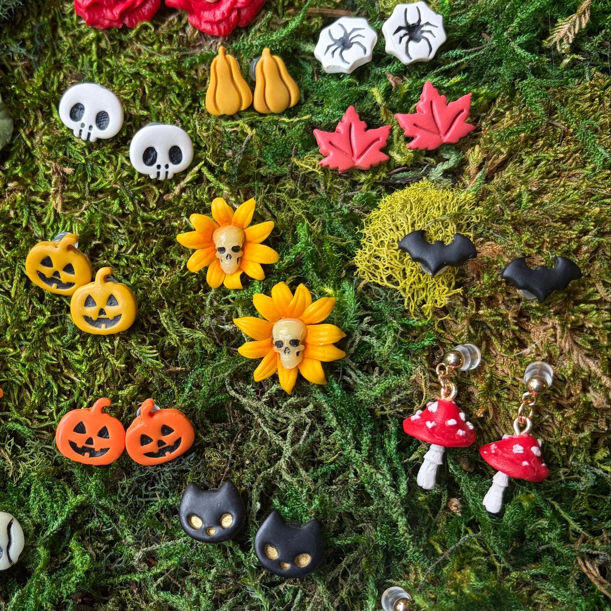 Bijoux d’Halloween en argile polymère sur un fond de mousse, avec des puces chauves-souris noires.