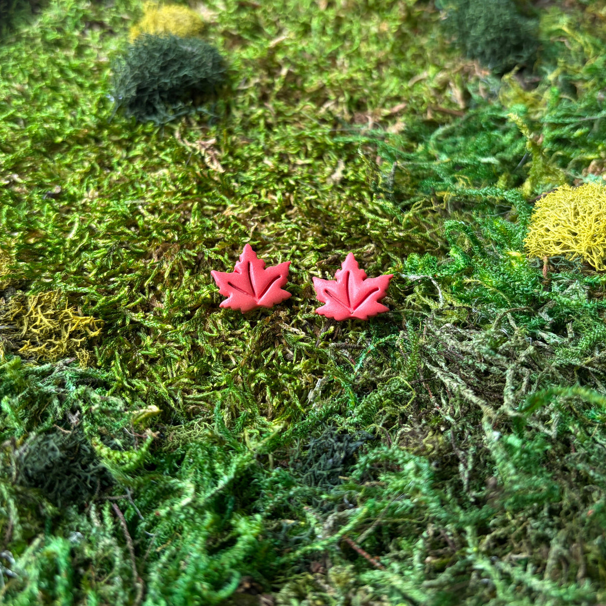 Deux puces feuilles d’érable en argile polymère aux teintes chaudes, posées sur la mousse.