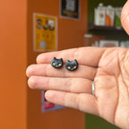 Paire de puces têtes de chats noirs aux yeux dorés, présentée dans une main.