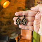 Paire de médaillons noirs ornés de champignons à finition dorée, suspendus à des clous boule noirs.