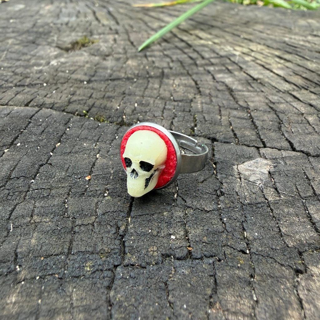 Bague à crâne sculpté ivoire et noir sur fond rouge, avec monture argentée.